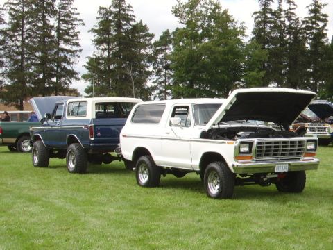 1978 Ford Bronco - Two classic Ford Broncos are displayed outdoors on a grassy field with trees in the background.