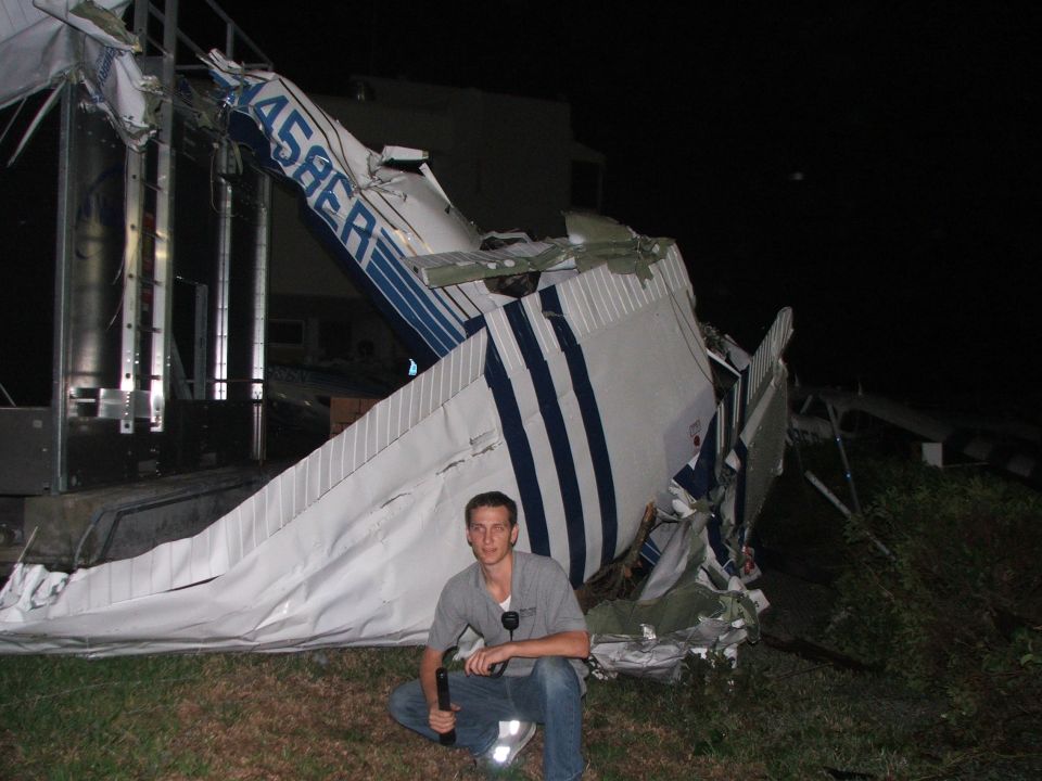 Man kneeling by wreckage of a crashed white and blue small airplane at night