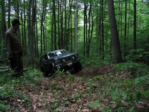 1986 Ford Bronco - A man stands near a dark green Ford Bronco navigating a wooded trail.