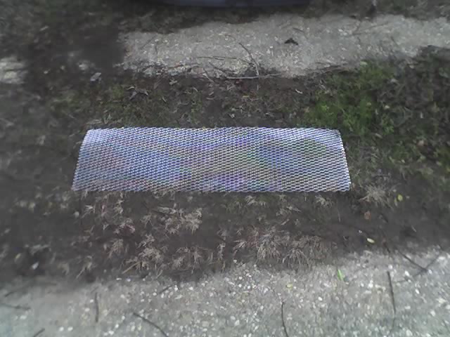 Rectangular piece of silver mesh, likely a car grille insert, lying on the ground
