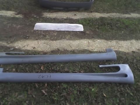 2000 Ford Escort - Car body kit parts, including side skirts and a bumper, laid out on the grass.