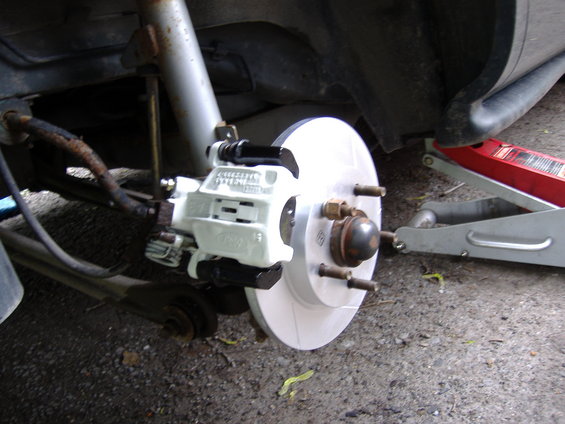 1998 Ford Taurus rear brake caliper and rotor assembly, white caliper, silver rotor, on a vehicle being serviced