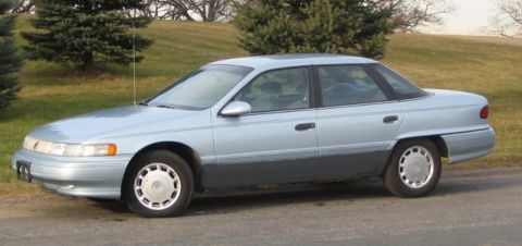 1993 Ford Taurus - A light blue 1993 Mercury Sable sedan is parked on the side of the road with trees in the background.