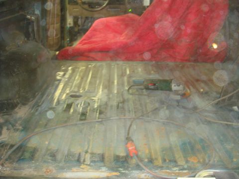1996 Ford Bronco - The interior floor of a vehicle shows signs of rust and is being prepped for repair with a grinder present.