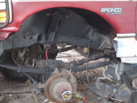 1989 Ford Bronco - The rear suspension and wheel well of a red Ford Bronco are shown with some components disassembled.