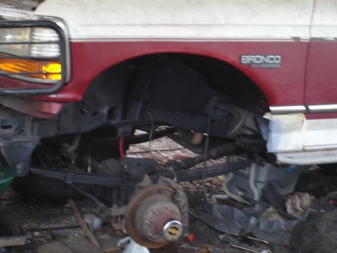 1989 Ford Bronco - The front fender and suspension of a red and white Ford Bronco are visible, suggesting it is in a state of repair.