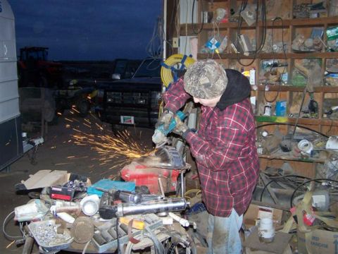 1995 Ford Bronco - A person grinds metal near a black Ford Bronco in a cluttered garage.