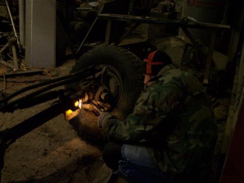 1995 Ford Bronco - A person is seen welding on a vehicle's axle and wheel assembly in a workshop setting.