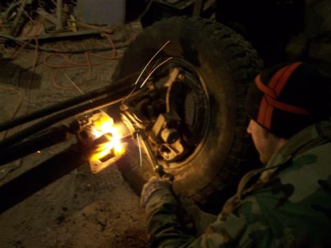 1995 Ford Bronco - Welding sparks fly as a person works on a vehicle's axle and wheel assembly.