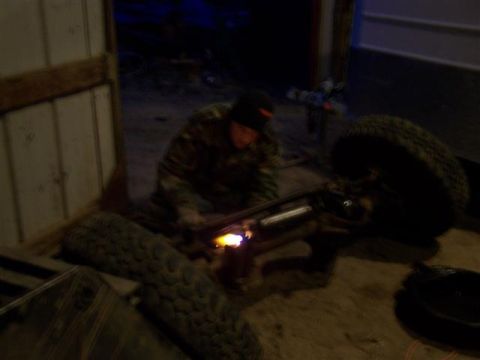 1995 Ford Bronco - A person is welding a part of a vehicle's axle in a dimly lit garage.