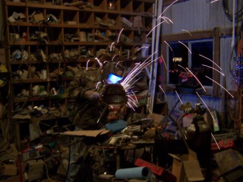 1995 Ford Bronco - A person is welding in a workshop filled with tools and parts, with sparks flying.