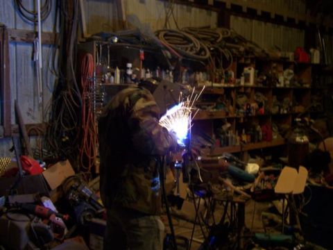 1995 Ford Bronco - A person welds in a workshop filled with tools, supplies, and electrical cords.