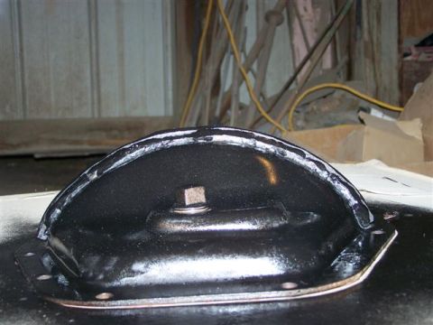 1995 Ford Bronco - A close-up view of a black metal automotive part, possibly a cover or bracket, with visible sealant and a bolt.