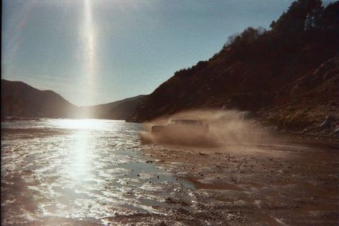 1988 Ford Bronco - A vehicle navigates a dusty, wet terrain under a bright sky.