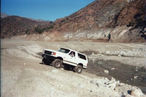1988 Ford Bronco - A white Ford Bronco navigates a rocky, off-road terrain with mountains in the background.