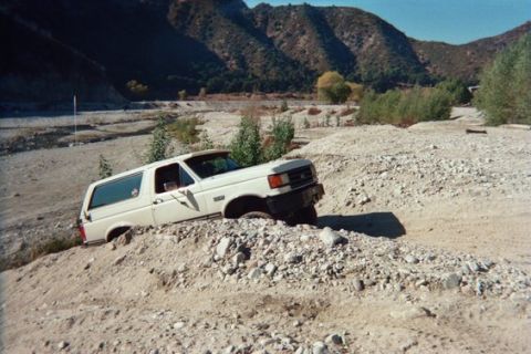 1988 Ford Bronco - White Ford Bronco is stuck in a dirt embankment in a dry riverbed.