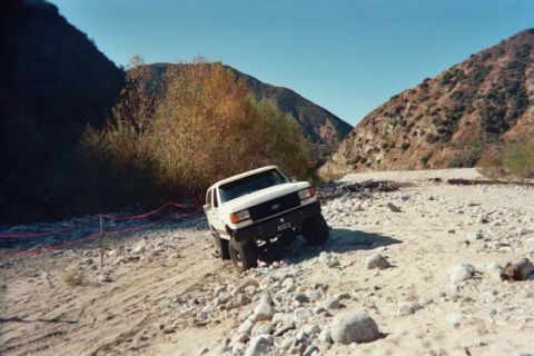 1988 Ford Bronco - A white Ford F-series truck navigates a challenging rocky terrain in a canyon.