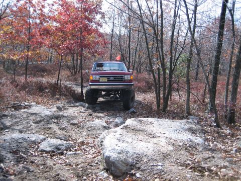 1990 Ford Bronco - A lifted red Ford Bronco navigates a challenging off-road course during autumn.