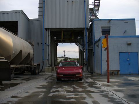 1991 Ford Probe - Head-on view of a red Ford Probe coupe parked under a bulk-loading spout at an industrial plant, framed by blue-painted steel structure and…