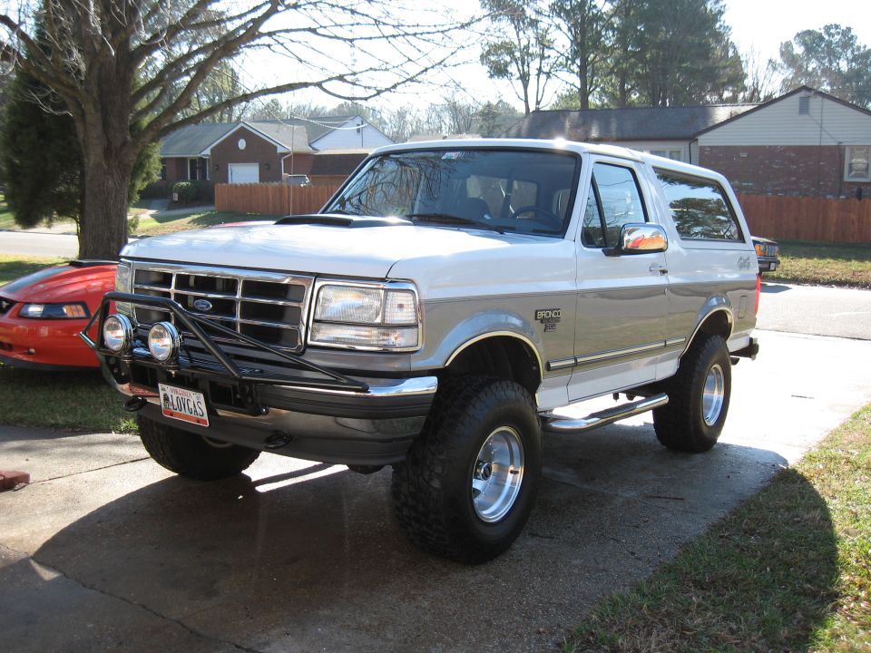 White lifted Ford Bronco XLT with brush guard and driving lights parked in a driveway