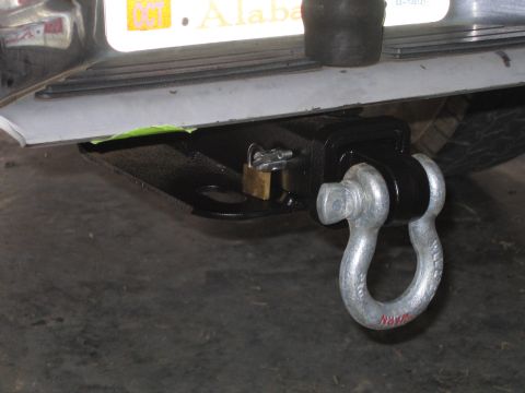 1989 Ford Bronco - Close-up of a trailer hitch assembly a shackle and a brass padlock, with a portion of an Alabama license plate above.