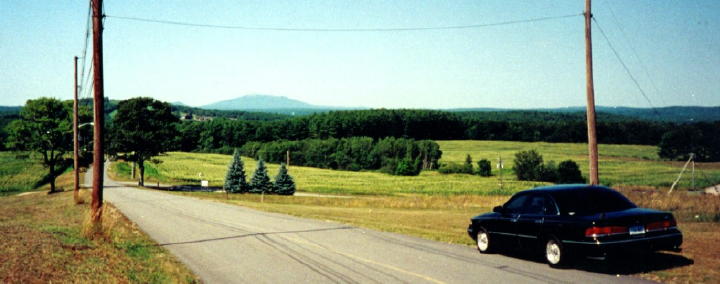 Black 1997 Ford Crown Victoria from rear, driving on a rural road