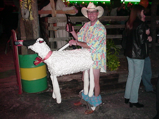 Man wearing a white sheep costume with a pink collar and red bow, holding a beer bottle