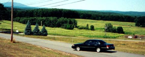 1997 Ford Crown Victoria - A black 1997 Ford Crown Victoria is seen from the side as it drives along a paved road in a rural setting.