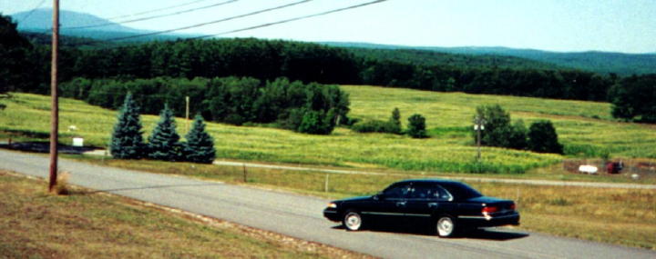 Black 1997 Ford Crown Victoria driving on a rural road with green hills in the background