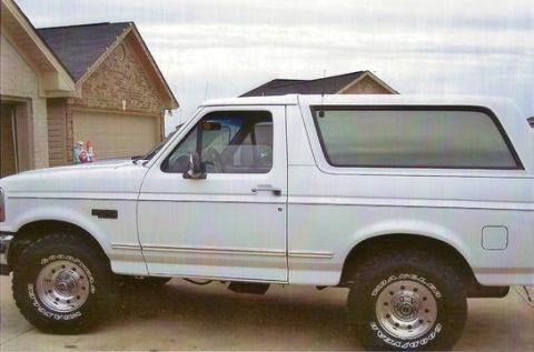 1995 Ford Bronco - Side profile of a white 1995 Ford Bronco parked in front of a brick house.
