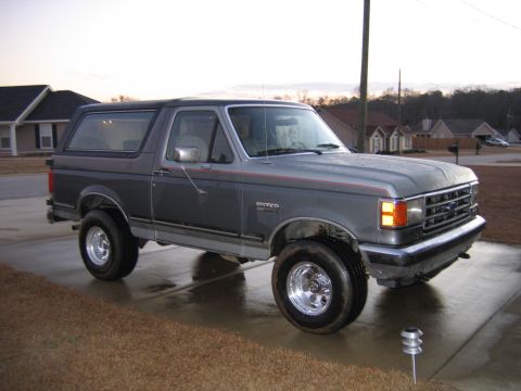 1989 Ford Bronco - Gray 1989 Ford Bronco with aftermarket wheels sits on a wet concrete driveway.
