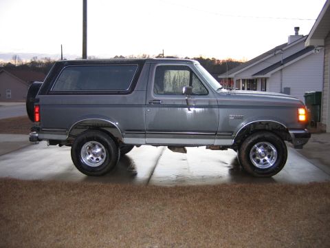1989 Ford Bronco - This gray Ford Bronco is parked on a concrete driveway in front of a house.
