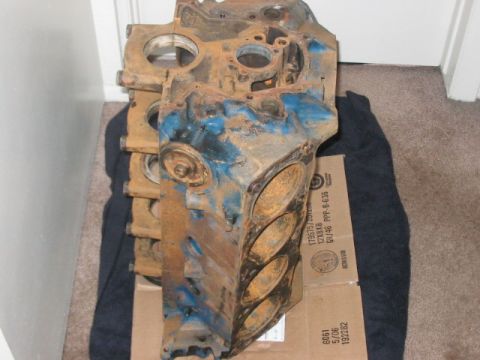 1991 Ford Bronco - A heavily rusted engine block, possibly for a Ford vehicle, shows signs of blue paint and has its cylinder bores exposed.
