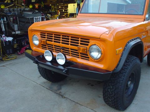 1977 Ford Bronco - This orange 1977 Ford Bronco is parked in a garage with another vehicle in the background.