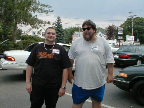 1997 Ford Crown Victoria - Two men pose for a photo in front of parked vehicles at an outdoor event.