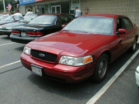 1997 Ford Crown Victoria - A red 1997 Ford Crown Victoria is parked in a lot, showing its front grille and headlights.