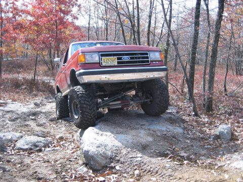 1990 Ford Bronco - 1990 Ford Bronco navigating a rocky off-road course in a wooded area.