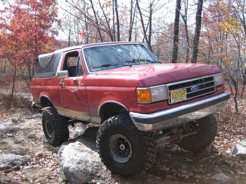 1990 Ford Bronco - A red Ford Bronco navigates a rocky off-road path during autumn.