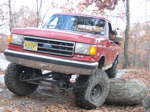 1990 Ford Bronco - Ford F-series truck with lifted suspension and large tires is shown off-roading over rocks.