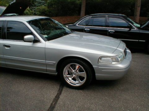 1997 Ford Crown Victoria - A silver sedan with aftermarket wheels is parked next to a black sedan.