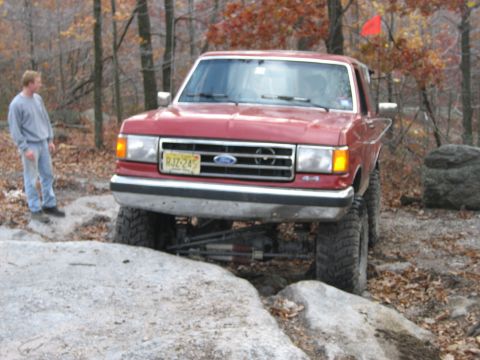 1990 Ford Bronco - This lifted Ford Bronco is shown off-roading over large rocks in a wooded area.