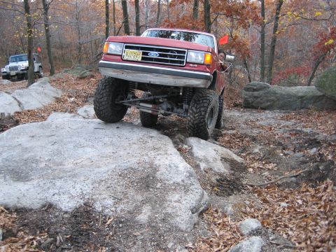 1990 Ford Bronco - A red Ford truck with off-road modifications tackles a challenging rock crawling course.
