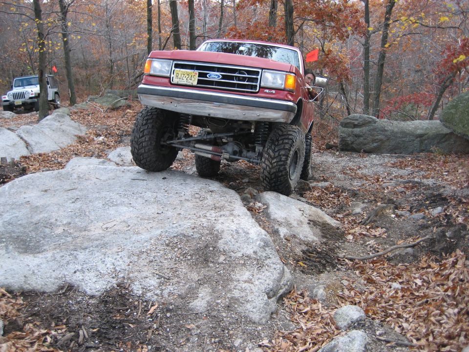 Red Ford F-Series truck with lifted suspension and large tires navigating rocky terrain