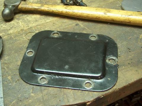 1991 Ford Bronco - A black metal plate with a raised center and six bolt holes is shown on a workbench.