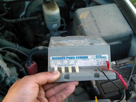 1986 Ford Bronco - A hand holds a remote pack strobe control unit, showing its four alternating outlets and input connections.