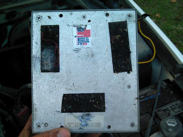 Hand holding an electronic control module with a "Made in USA" sticker and part number visible