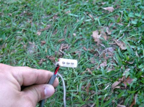 1986 Ford Bronco - Exposed electrical wires and a connector are held in a hand against a backdrop of grass and fallen leaves.