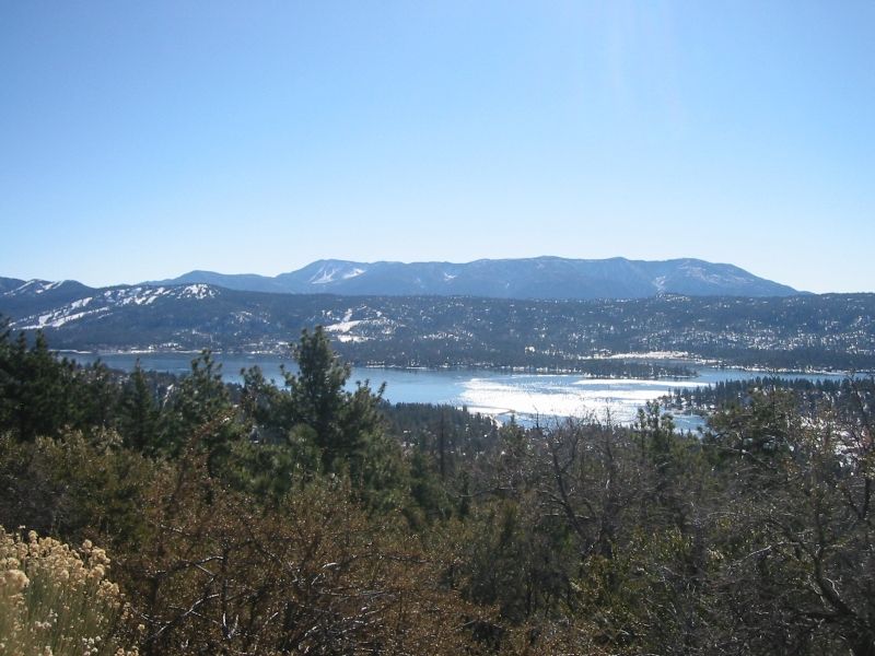 Overlook of a mountain lake with snow-streaked ridges and pines in the foreground
