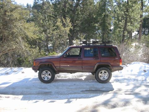 2000 Jeep Cherokee - Side view of a maroon 2000 Jeep Cherokee with a roof rack, parked on a snowy road with trees in the background.