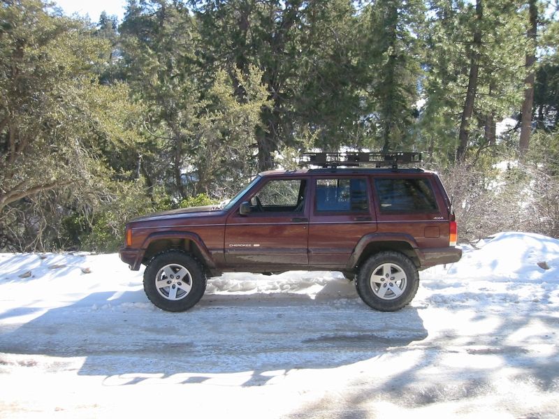Maroon four-door Jeep Cherokee XJ with roof rack parked on a snowy forest road